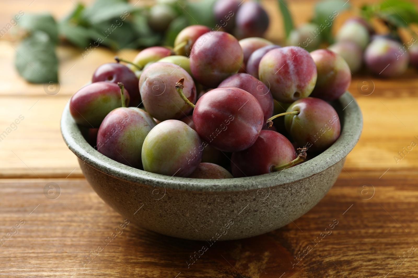 Photo of Ripe plums in bowl on wooden table, closeup