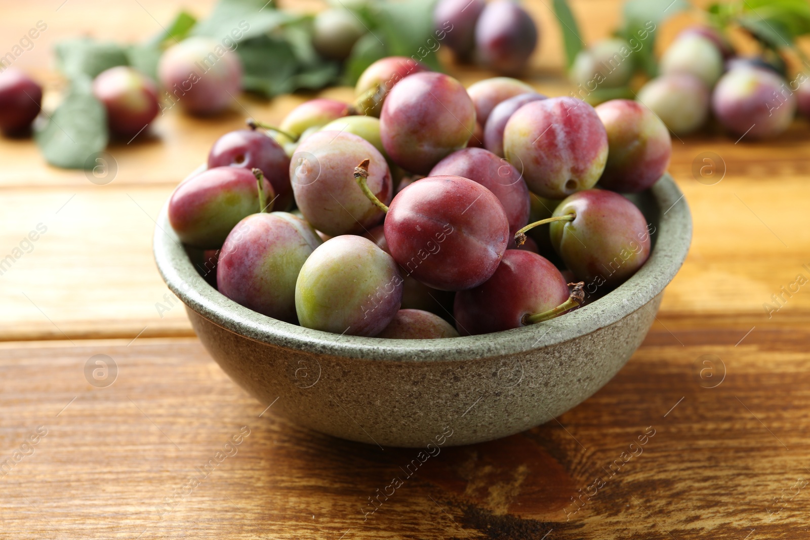 Photo of Ripe plums in bowl on wooden table, closeup