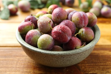 Photo of Ripe plums in bowl on wooden table, closeup