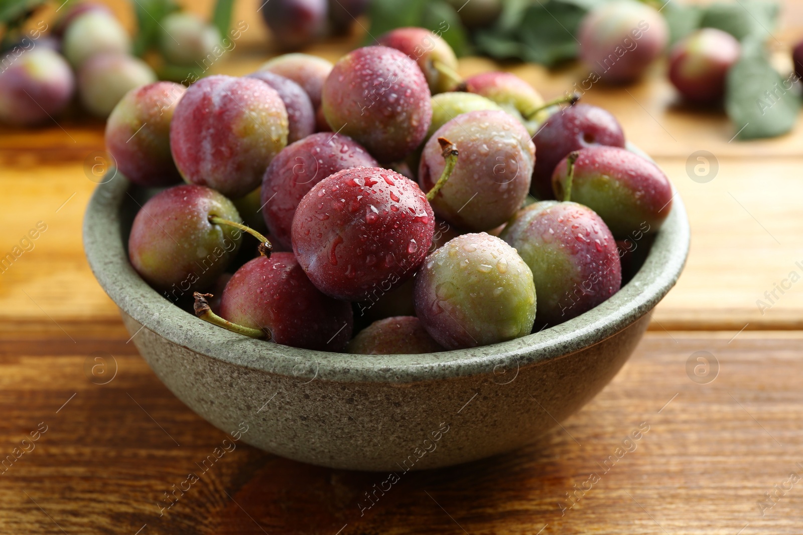 Photo of Ripe plums in bowl on wooden table, closeup