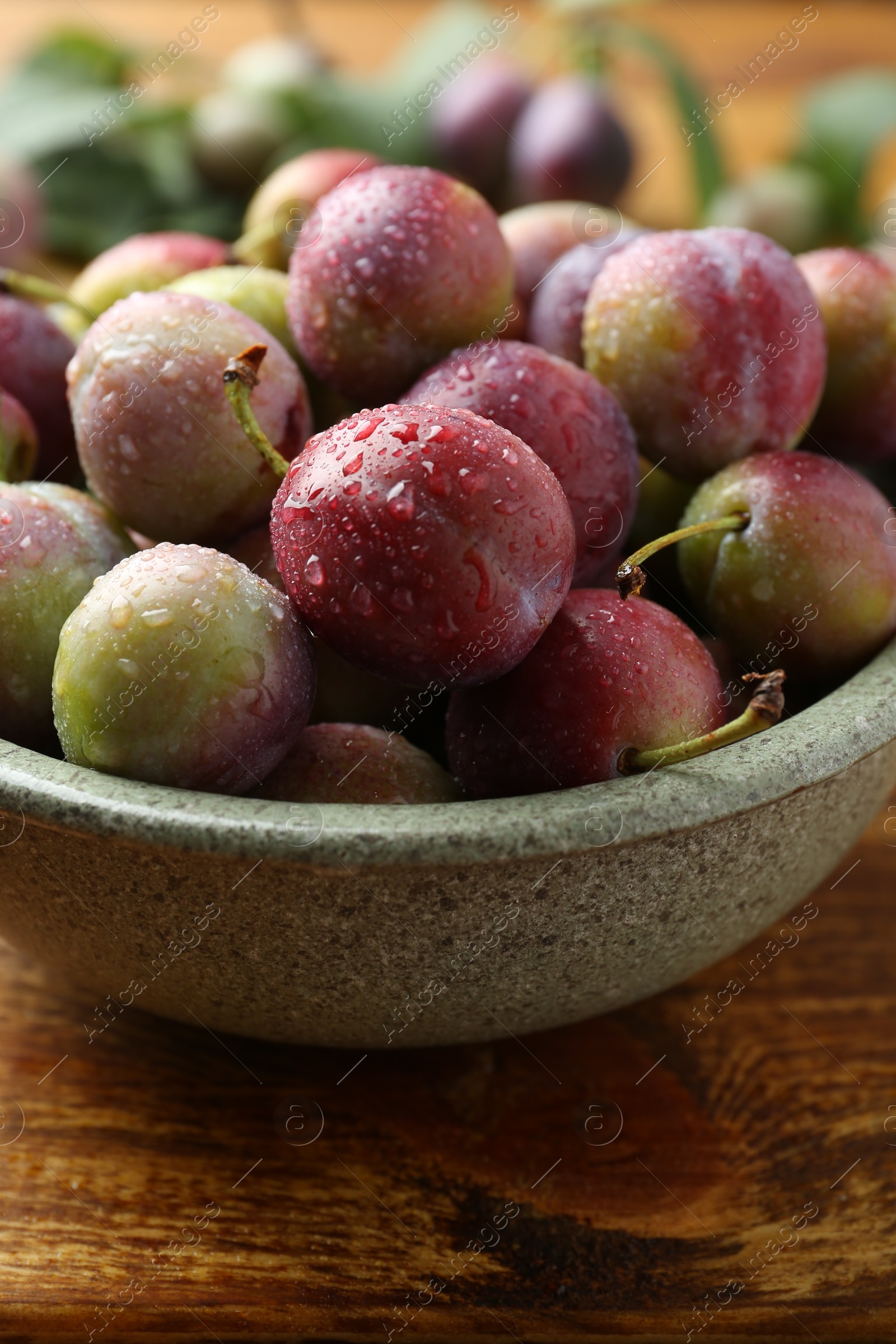 Photo of Ripe plums in bowl on wooden table, closeup