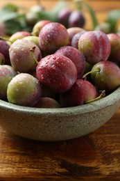 Photo of Ripe plums in bowl on wooden table, closeup