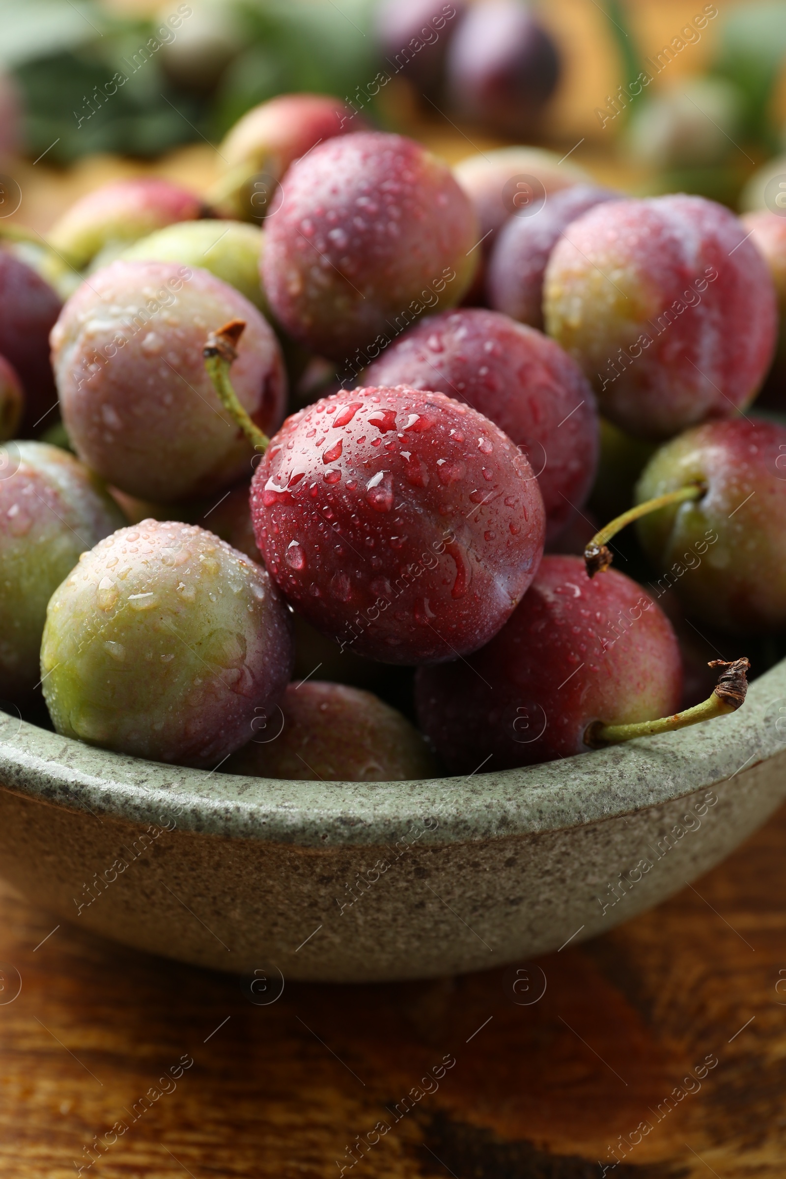 Photo of Ripe plums in bowl on wooden table, closeup