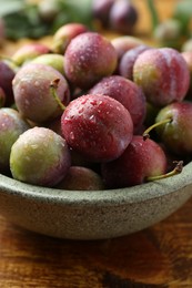 Photo of Ripe plums in bowl on wooden table, closeup