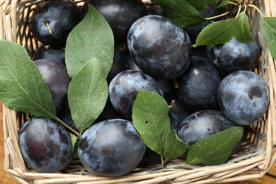 Photo of Tasty ripe plums and leaves in wicker basket, flat lay