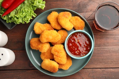 Photo of Hot chili sauce and nuggets served on wooden table, flat lay