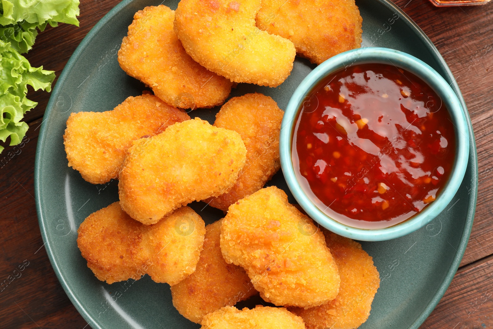 Photo of Plate with hot chili sauce and nuggets on wooden table, top view