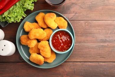 Photo of Plate with hot chili sauce and nuggets on wooden table, flat lay. Space for text