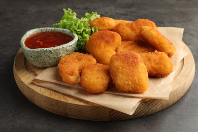 Photo of Board with hot chili sauce, lettuce and nuggets on grey textured table, closeup