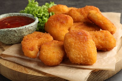 Photo of Board with hot chili sauce, lettuce and nuggets on table, closeup