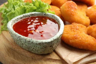 Photo of Hot chili sauce, lettuce and nuggets on wooden board, closeup