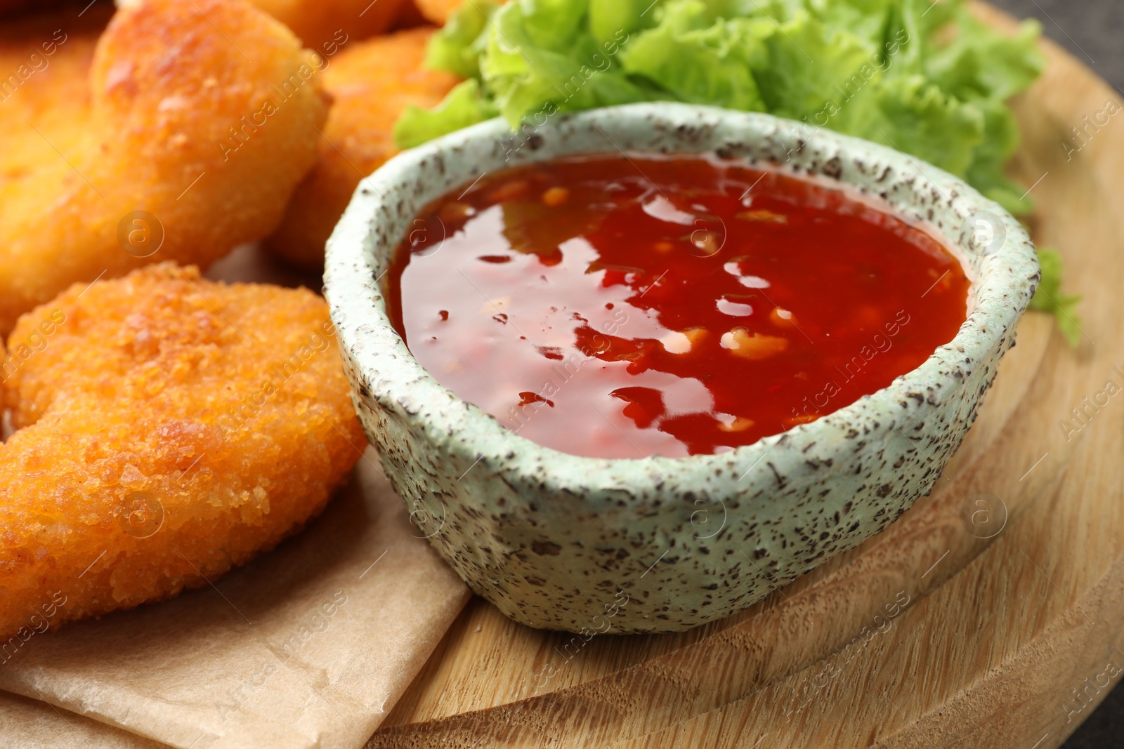 Photo of Hot chili sauce, lettuce and nuggets on wooden board, closeup