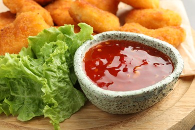 Photo of Hot chili sauce, lettuce and nuggets on wooden board, closeup