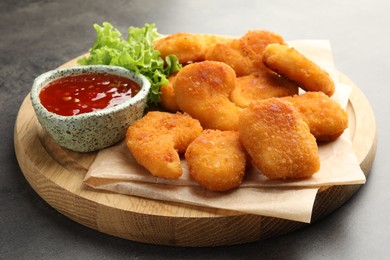 Photo of Board with hot chili sauce, lettuce and nuggets on grey textured table, closeup