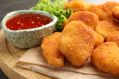 Photo of Hot chili sauce, lettuce and nuggets on wooden board, closeup