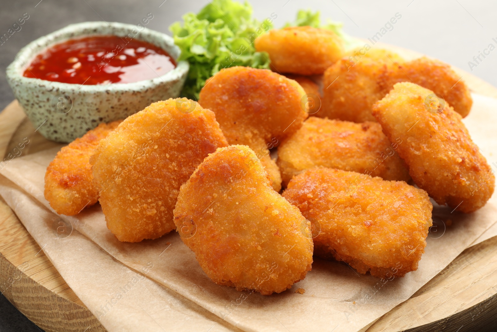 Photo of Board with hot chili sauce, lettuce and nuggets on table, closeup