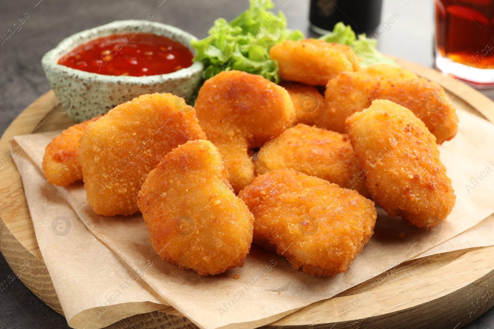 Photo of Board with hot chili sauce, lettuce and nuggets on table, closeup