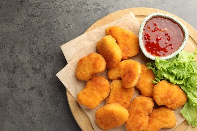 Photo of Board with hot chili sauce, lettuce and nuggets on grey textured table, top view. Space for text