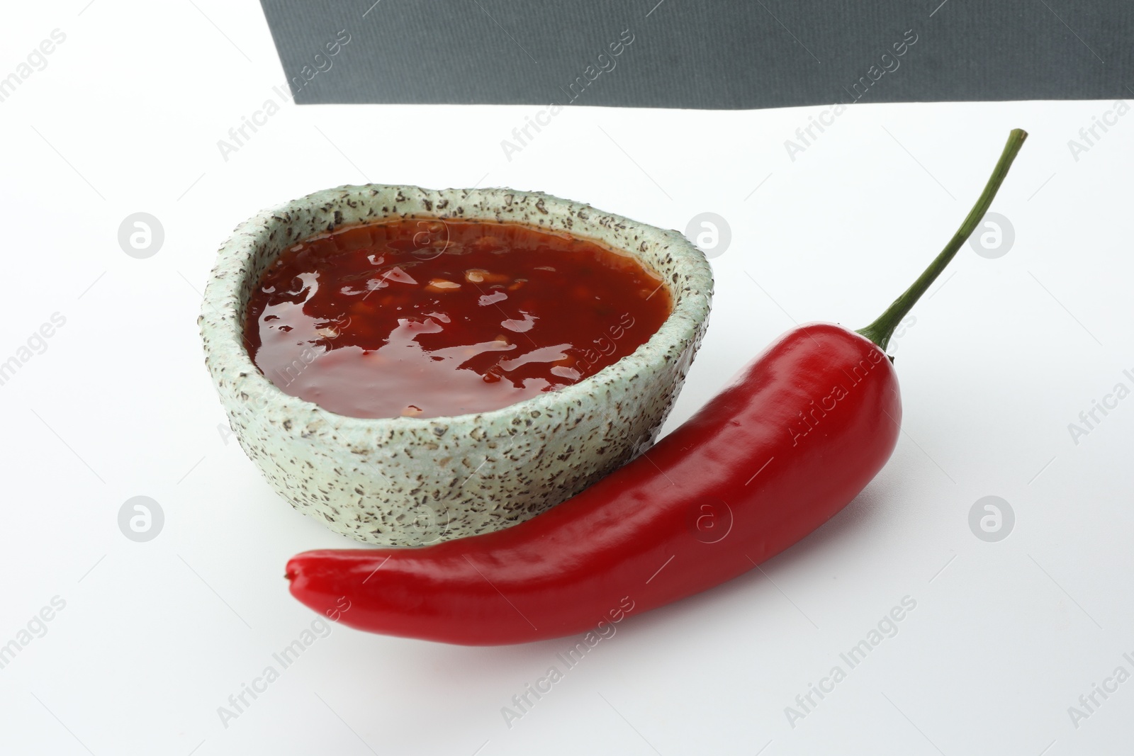 Photo of Hot chili sauce in bowl and pepper on white background