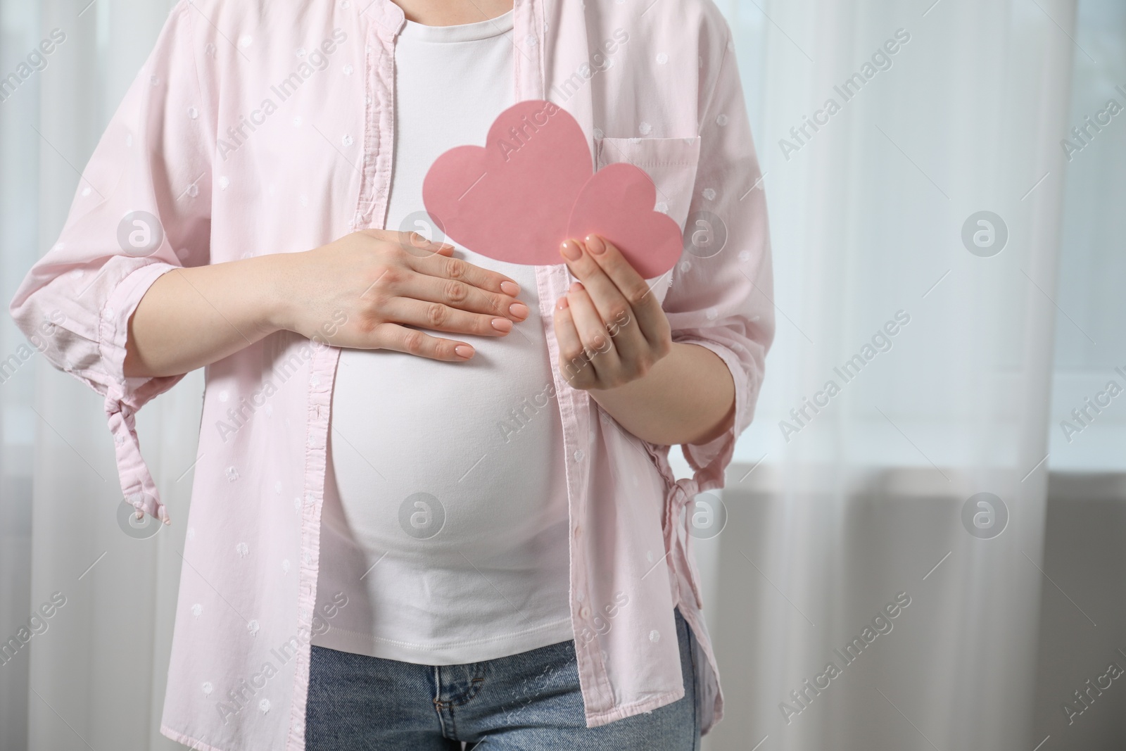 Photo of Expecting twins. Pregnant woman holding two paper cutouts of hearts at home, closeup. Space for text