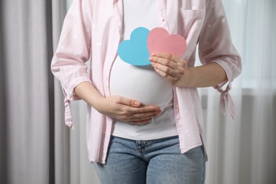 Photo of Expecting twins. Pregnant woman holding two paper cutouts of hearts at home, closeup