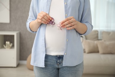 Expecting twins. Pregnant woman holding two pacifiers at home, closeup