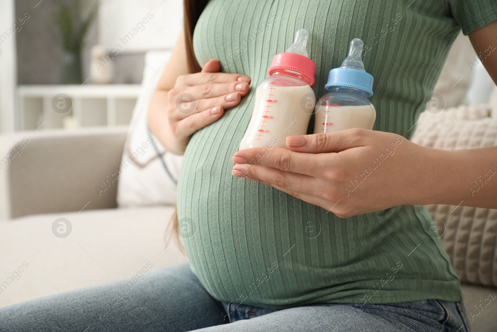 Photo of Expecting twins. Pregnant woman holding two bottles of milk at home, closeup