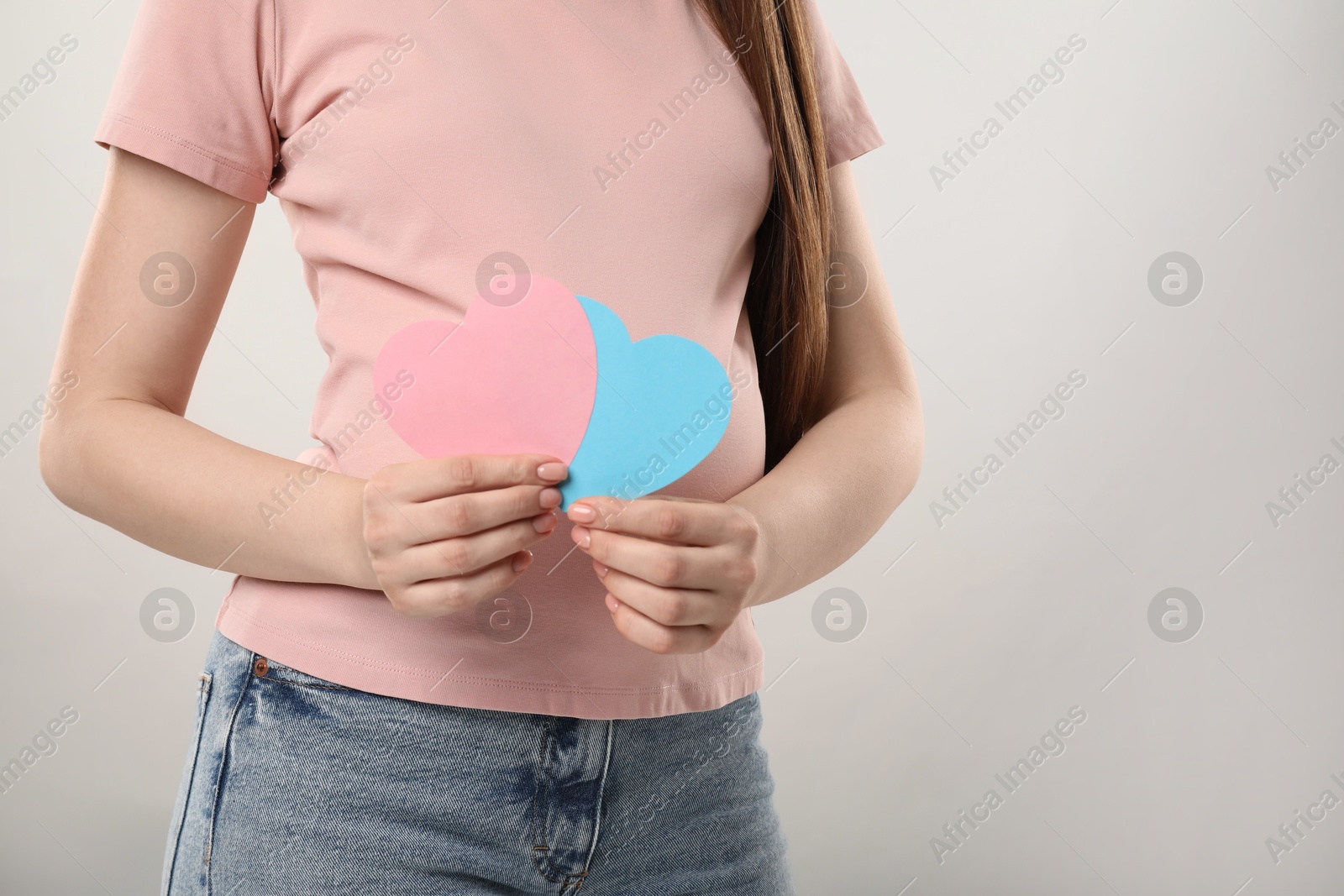 Photo of Expecting twins. Pregnant woman holding two paper cutouts of hearts on light grey background, closeup. Space for text