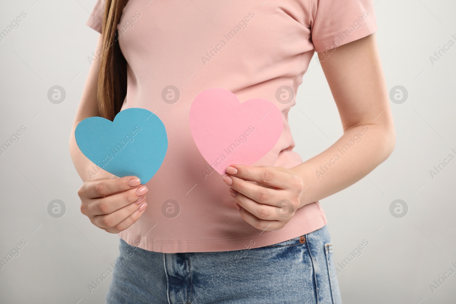 Photo of Expecting twins. Pregnant woman holding two paper cutouts of hearts on light grey background, closeup