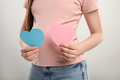 Expecting twins. Pregnant woman holding two paper cutouts of hearts on light grey background, closeup