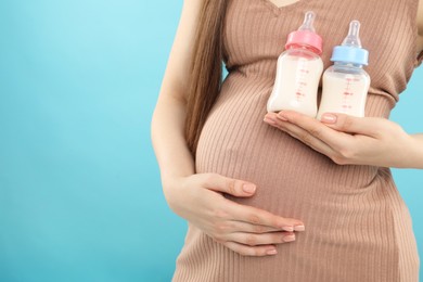 Photo of Expecting twins. Pregnant woman holding two bottles with milk on light blue background, closeup. Space for text