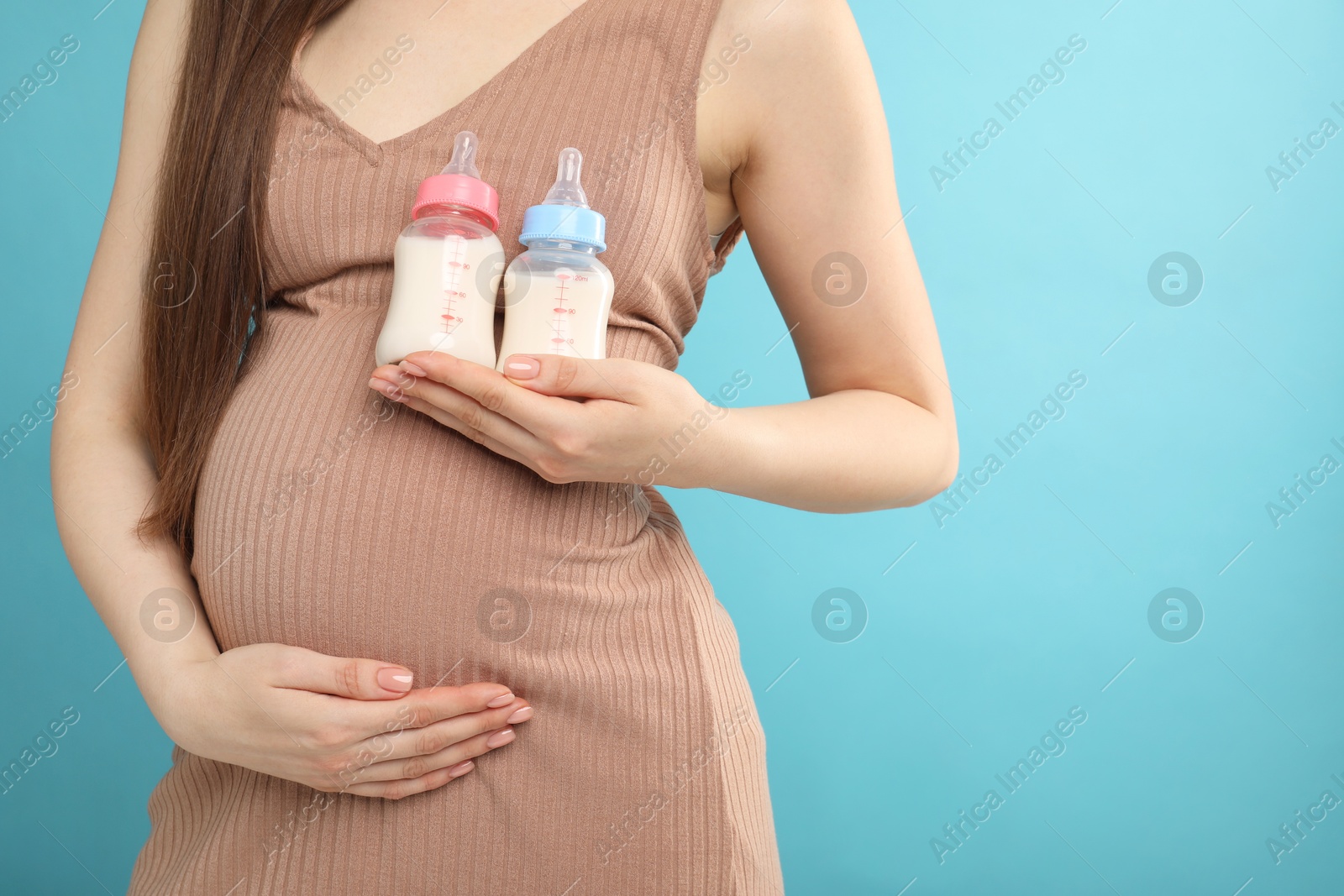 Photo of Expecting twins. Pregnant woman holding two bottles with milk on light blue background, closeup. Space for text