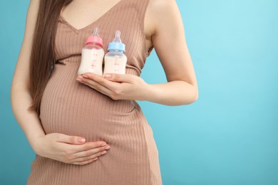 Photo of Expecting twins. Pregnant woman holding two bottles with milk on light blue background, closeup. Space for text