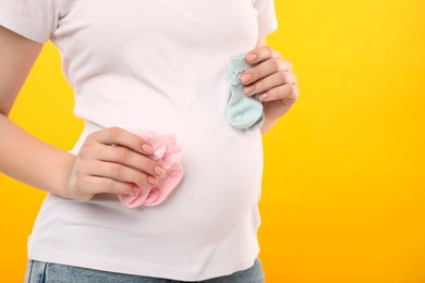 Expecting twins. Pregnant woman holding two pairs of socks on yellow background, closeup. Space for text