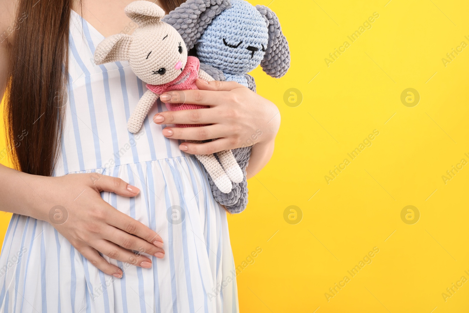 Photo of Expecting twins. Pregnant woman holding two toys on yellow background, closeup. Space for text