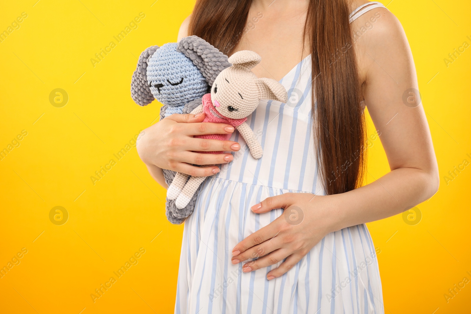 Photo of Expecting twins. Pregnant woman holding two toys on yellow background, closeup