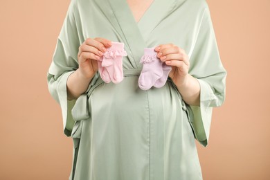 Expecting twins. Pregnant woman holding two pairs of socks on light brown background, closeup