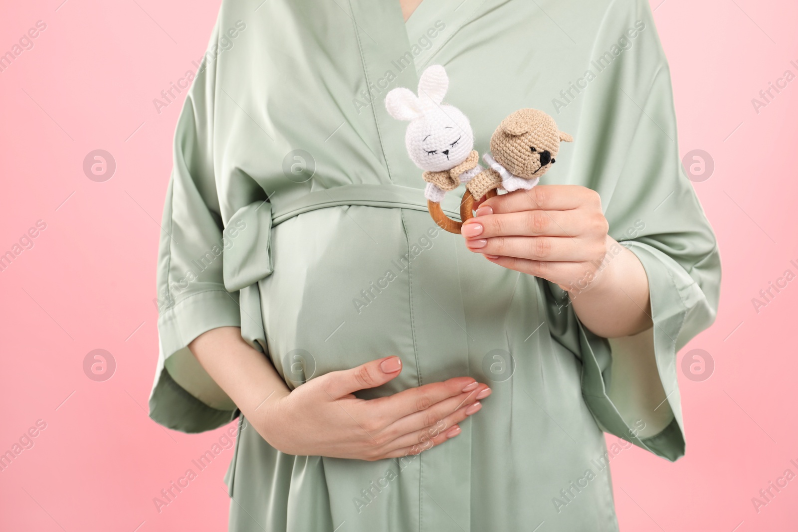 Photo of Expecting twins. Pregnant woman holding two toys on pink background, closeup