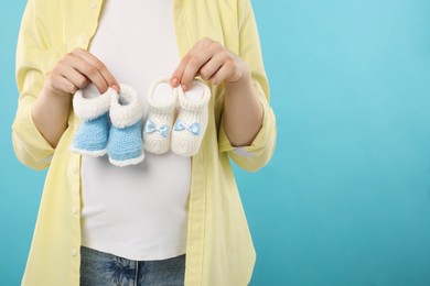 Photo of Expecting twins. Pregnant woman holding two pairs of baby shoes on light blue background, closeup. Space for text