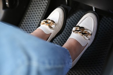 Photo of Woman in white shoes pushing on pedal of car brake, closeup