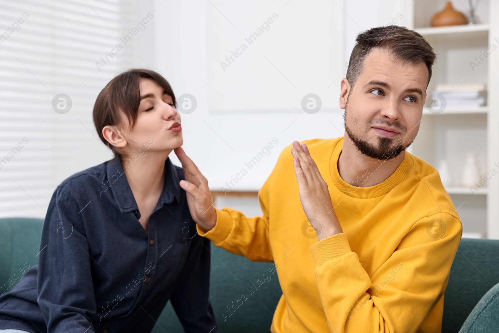 Photo of Embarrassed man refusing from woman's kiss at home