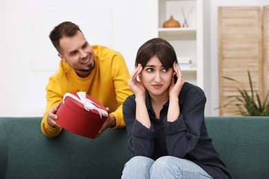 Smiling man presenting gift to embarrassed woman at home