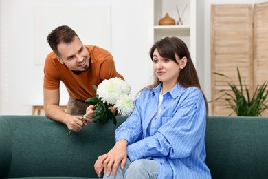 Photo of Smiling man presenting flowers to embarrassed woman at home