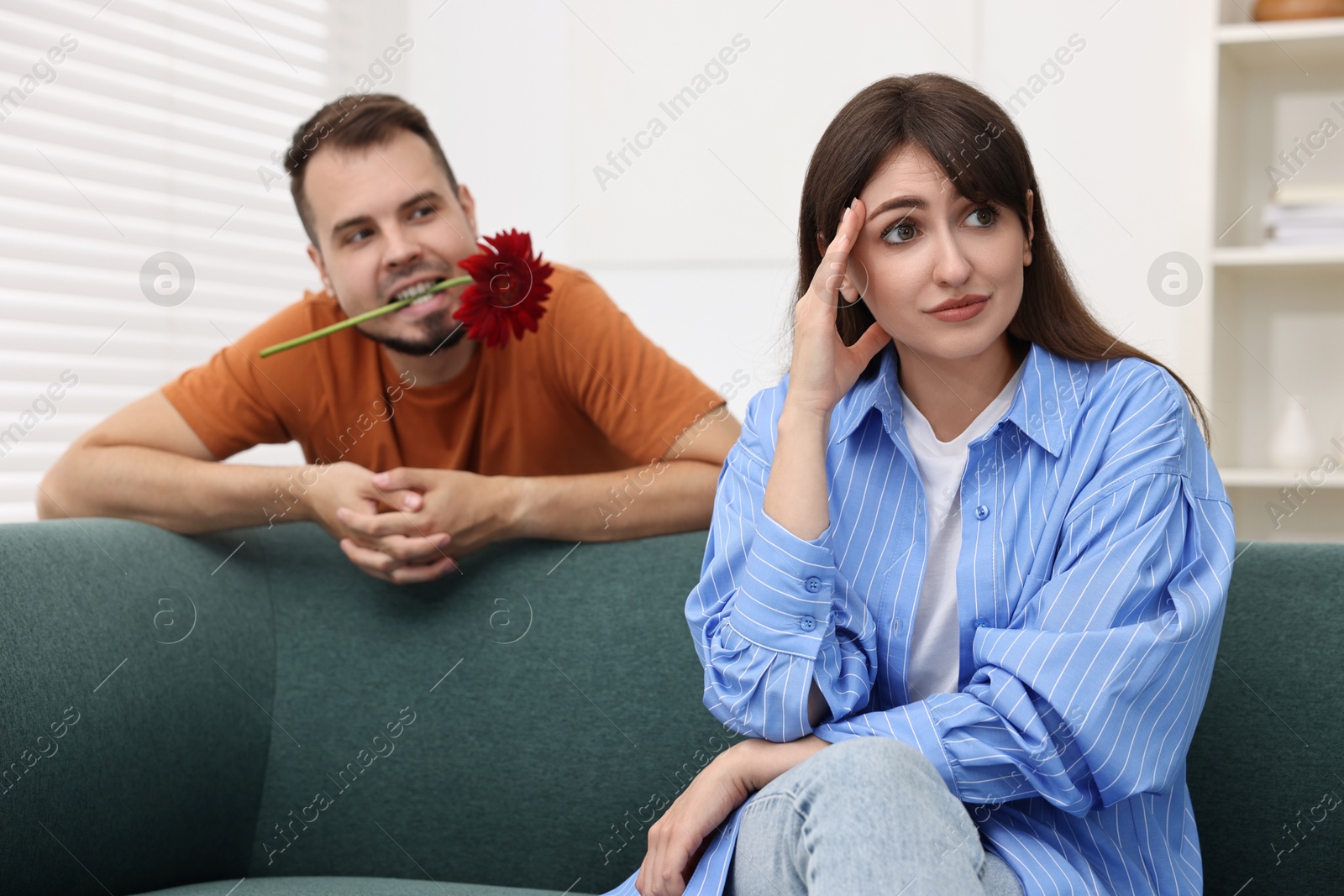 Photo of Man with flower in mouth flirting with embarrassed woman at home