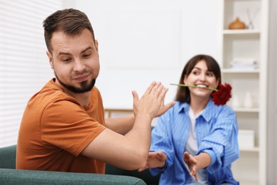 Woman with flower in mouth flirting with embarrassed man at home, selective focus