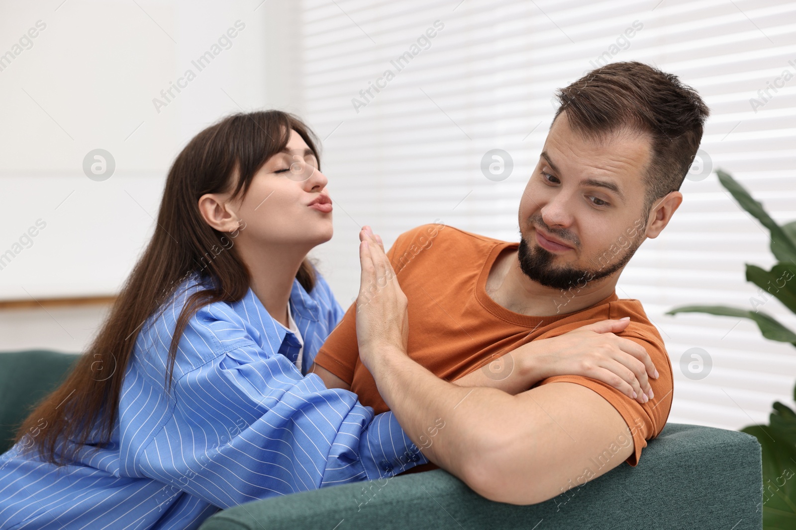 Photo of Embarrassed man refusing from woman's kiss at home