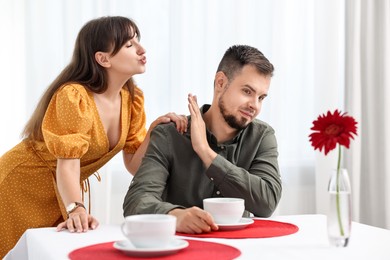 Bad date. Embarrassed man refusing from woman's kiss indoors