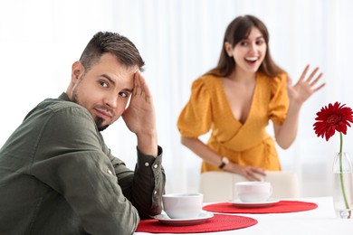 Bad date. Embarrassed man ignoring smiling woman indoors, selective focus