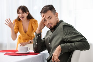 Bad date. Embarrassed man ignoring smiling woman indoors, selective focus