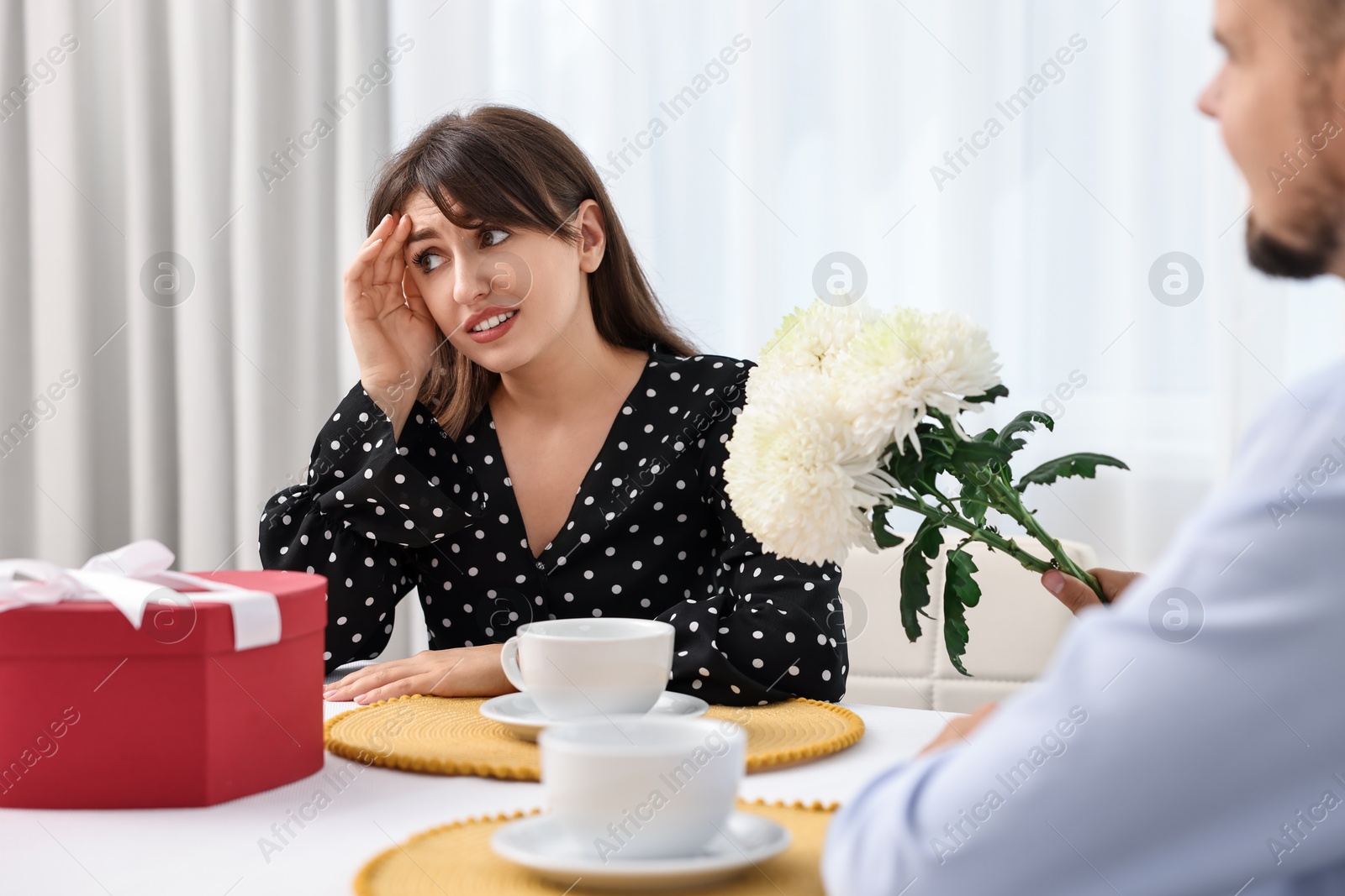 Photo of Bad date. Embarrassed woman ignoring man with flowers indoors